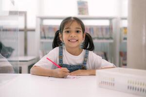 A young girl is sitting at a desk with a red crayon in her hand photo