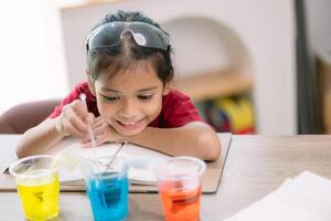 Asian girl making Walking Water experiment. Food color is added to the water in the glass, water moves along the paper, and then color is mixed. Concept of science for kid photo