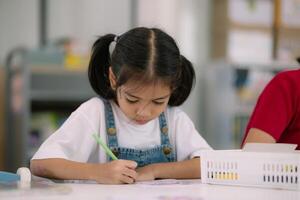 A young girl is sitting at a table with a green crayon in her hand photo