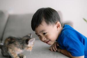 un joven chico es mirando a un gato en un sofá foto