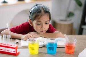 Asian girl making Walking Water experiment. Food color is added to the water in the glass, water moves along the paper, and then color is mixed. Concept of science for kid photo