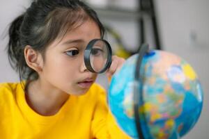 un joven niña es mirando a un globo mediante un aumentador vaso foto