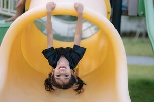 A young girl is hanging upside down on a yellow slide photo