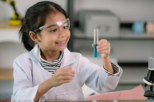 Little cute girl with a microscope holding a laboratory bottle with water experiment study scientists at school. Education science concept. photo