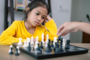 un niña en un amarillo camisa es jugando un juego de ajedrez con otro persona foto