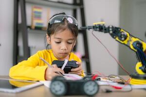 A young girl is sitting at a table with a robot and a remote control photo