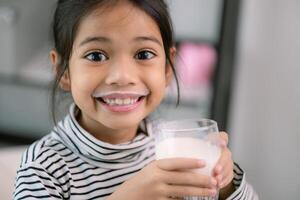 Asian little cute girl drinking milk  Young preschool child girl or daughter stays home with a smiling face, feels happy, and enjoys drinking milk. photo