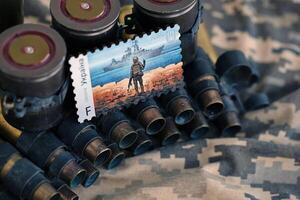 TERNOPIL, UKRAINE - SEPTEMBER 29, 2023 Famous Ukrainian postmark with russian warship and ukrainian soldier as wooden souvenir on army camouflage uniform cloth and machine gun belt photo