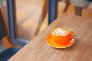 Hot latte coffee in orange color cup on wooden table photo