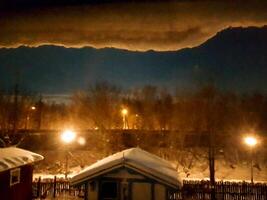 The houses covered with snow and the street lamps that can be seen from the window after the snowfall in digital painting style photo