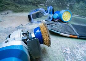 ángulo amoladora con latón cable cepillo cabeza a fregar el pared superficie y antipolvo equipo, gafas de protección y cuero guantes para el la seguridad de el cuerpo. foto