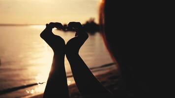 Love. Beautiful girl with long hair makes a beautiful heart symbol with both hands during sunset at sea. The style of cinema. HD. video