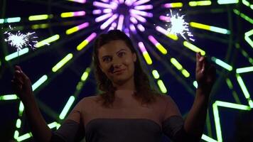 Beautiful happy girl with long hair holds fireworks in hands on a background of multi-colored lights having a good mood at night. slow motion video