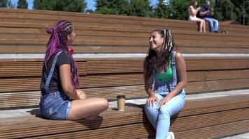 two beautiful girlfriends talking to each other sitting on a bench in the park. slow motion video