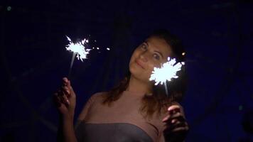schön glücklich Mädchen mit lange Haar hält Feuerwerk im Hände auf ein Hintergrund von mehrfarbig Beleuchtung haben ein gut Stimmung beim Nacht. schleppend Bewegung. hd video