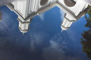 View of the White Mosque with water reflections on the road against a blue sky background photo