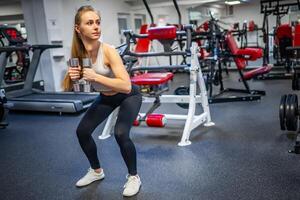 joven mujer sostiene pesas en su manos y trabajos fuera en el gimnasio ejecutando un ejercicio foto