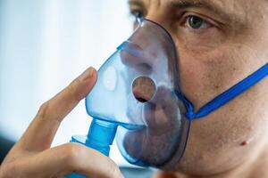 Close up view of unhealthy man wearing nebulizer mask in home. Health, medical equipment and people concept. High quality photo