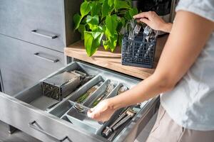 mujer ama de casa manos ordenar arriba cuchillería después lavavajillas máquina. mujer pulcramente montaje tenedor, cuchara, cuchillo accesorios para almacenamiento organización foto