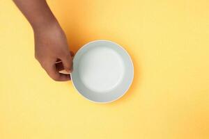 Woman's hand holding an empty green plate on a yellow background with copy space. Healthy eating, diet concept. Banner photo