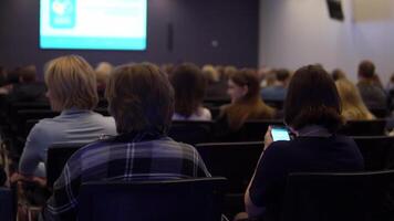 A large group of people at a conference on the development and promotion of business are listening to business coaches. back view. video