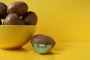 Still life of fruit trending illuminatiited yellow kiwi in a bowl plate of yellow and next pieces of kiwi yellow background with a place to text copyspace photo