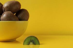 todavía vida Fruta en un amarillo cuenco plato en un amarillo antecedentes siguiente a mentiras un pedazo de kiwi iluminado amarillo tendencia color copyspace foto