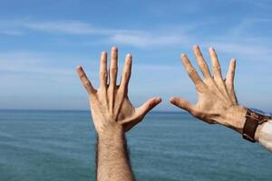 mano haciendo, mostrando número diez gesto símbolo en azul verano cielo naturaleza antecedentes. gesticulando número 10 número diez en firmar idioma.diez dedos arriba foto