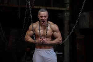 Primal instinct. Angry muscular man screaming at camera and breaking chains on chest photo