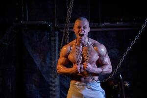 Primal instinct. Angry muscular man screaming at camera and breaking chains on chest photo