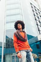 Young curly black African American with glasses walks through the city streets against a skyscraper photo