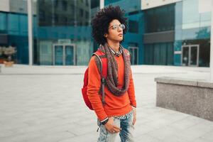 Young curly black African American with glasses walks through the city streets against a skyscraper photo