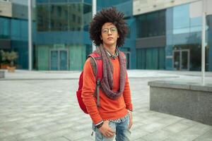 Young fashionable dressed curly black African American with glasses walks through the streets against a skyscraper. photo