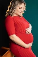 Pregnant Woman Posing In An Elegantred Dress indoors studio green wall background photo