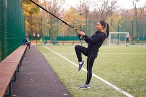 Girl athlete training using trx on sportground. Mixed race young adult woman do workout with suspension system. Healthy lifestyle. Stretching outdoors playground. photo