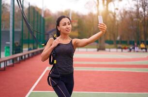 Girl athlete training using  on sportground. Mixed race young adult woman do workout with suspension system. Healthy lifestyle. Stretching outdoors playground. photo