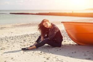 A girl sideways near a red boat on the beach by the sea photo
