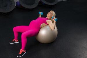 Pregnant woman exercise withdumbbells on fitness bal in gym photo