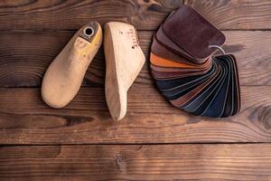 Leather samples for shoes and wooden shoe last on dark wooden table. photo
