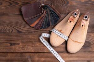 Leather samples for shoes and wooden shoe last on dark wooden table. photo