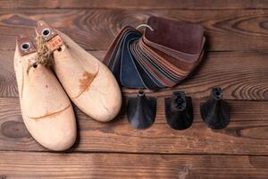 Leather samples for shoes and wooden shoe last on dark wooden table. photo