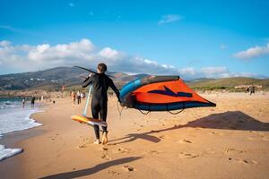 Man with kite hydrofoil equipment walking sandy beach photo