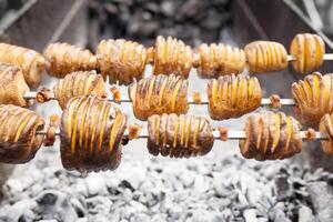 A shish kebab from yellow potatoes put on a skewer is fried on blue coals photo