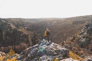 viajero en un amarillo chaqueta en pie en el borde de un rock disfrutando un momento de relajación y un ver de el divorciar sarcasmo valle, praga, checo república. lograr éxito foto