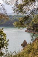 View from pine trees on lake with clean water and surrounding beautiful mountains in sunny day. Doyran Pond, Antalya, Turkey. photo