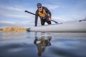 mayor palista y su paddleboard en lago en invierno o temprano primavera en Colorado, rana perspectiva, parcialmente sumergido acción cámara foto