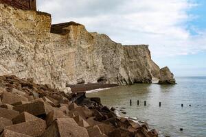 Dramatic chalk cliffs with boulder-strewn beach and calm sea under a cloudy sky. photo