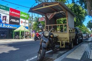 a three-wheeled pick-up motorbike or commonly called a tossa parked on the side of an urban road with a billboard in the background containing various advertisements, Indonesia, 17 September 2023. photo