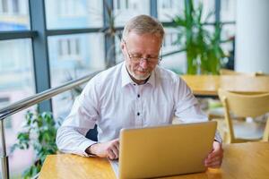 Senior stylish business man in the ofiice. Confident and concentrated. Thoughtful mature man looking at his laptop at his working place. photo