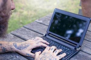manos de un tatuado hombre trabajando con computadora al aire libre foto